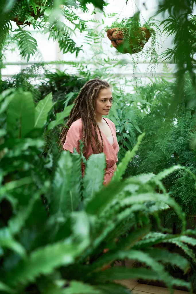 Selective focus photo of a woman standing amidst lush plants.